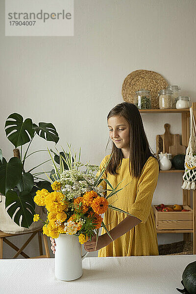 Lächelndes Mädchen mit Blumenvase  das zu Hause am Tisch in der Küche steht