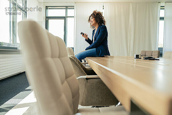 Reife Geschäftsfrau mit Smartphone sitzt am Konferenztisch im Büro