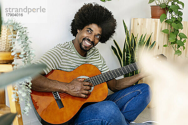 Glücklicher Mann mit Afro-Frisur  der zu Hause Gitarre übt