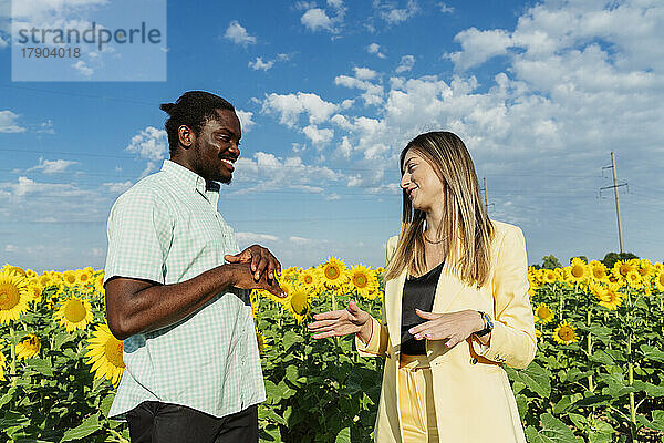Lächelnde Geschäftsfrau im Gespräch mit Kollegen im Sonnenblumenfeld