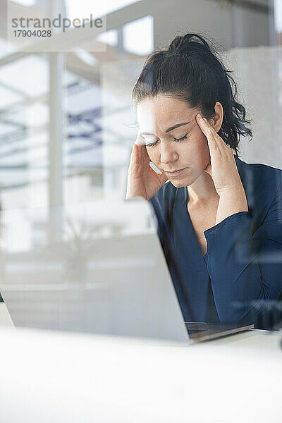 Geschäftsfrau mit Kopf in den Händen sitzt vor Laptop auf dem Tisch