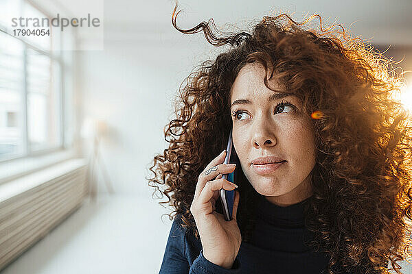 Schöne Frau mit lockigem Haar  die auf dem Smartphone spricht und nachdenkt