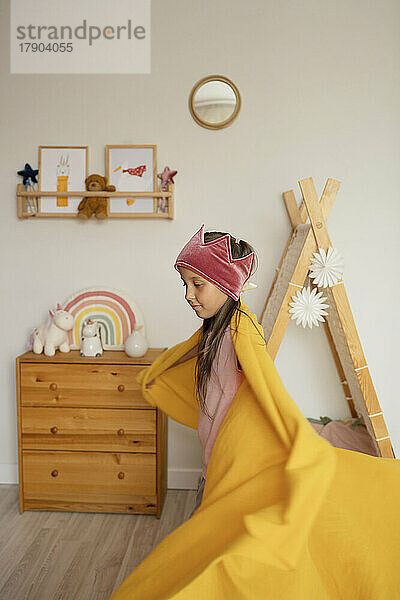 Girl wrapped in blanket playing at home