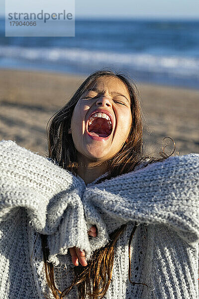 Fröhliches Mädchen schreit an einem sonnigen Tag am Strand