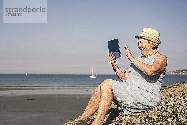Glückliche ältere Frau winkt bei einem Videoanruf am Strand
