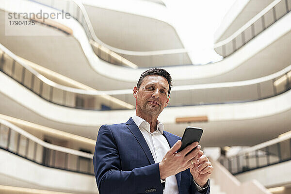 Selbstbewusster reifer Geschäftsmann mit Smartphone in der Lobby
