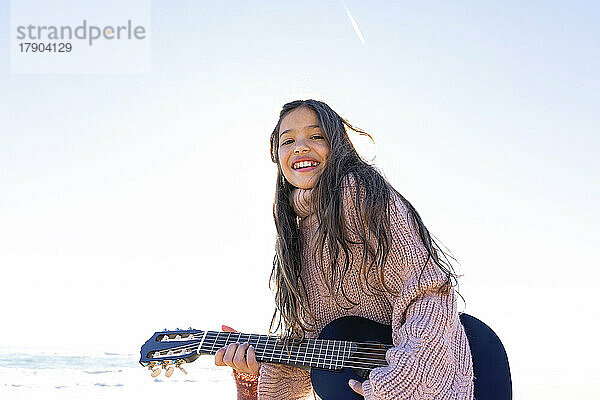 Glückliches Mädchen  das an einem sonnigen Tag am Strand Gitarre spielt
