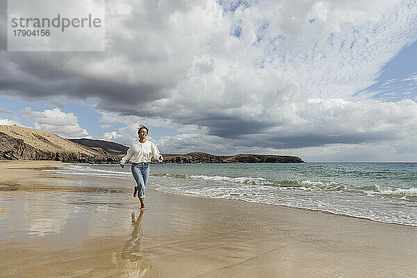 Junge Frau läuft am Strand entlang der Küste