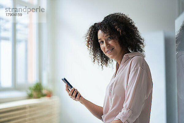 Lächelnde Geschäftsfrau mit Mobiltelefon am Arbeitsplatz