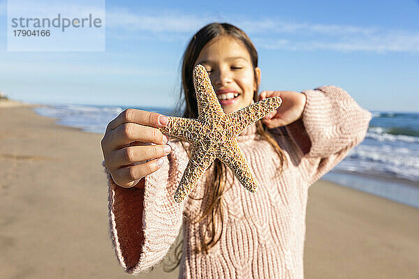 Lächelndes Mädchen zeigt Seesterne am Strand an einem sonnigen Tag