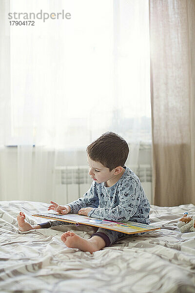 Junge liest Buch auf dem Bett