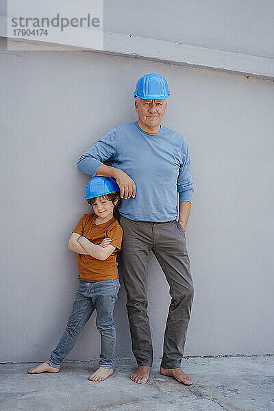 Selbstbewusster Großvater und Enkel mit Helm vor der Wand
