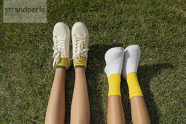 Girls wearing white shoes relaxing on grass at park
