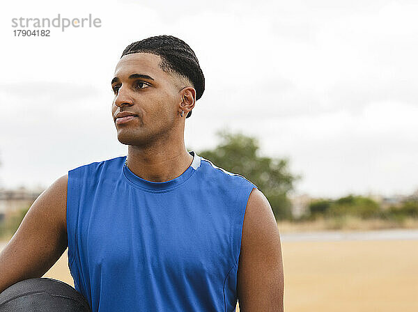 Nachdenklicher junger Mann mit Basketball am Sportplatz