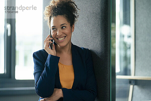 Glückliche Geschäftsfrau  die im Büro mit dem Mobiltelefon spricht