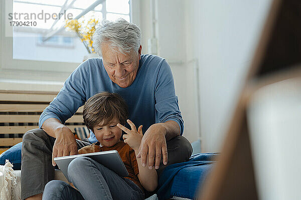 Glücklicher Junge  der zu Hause einen Tablet-PC mit seinem Großvater teilt