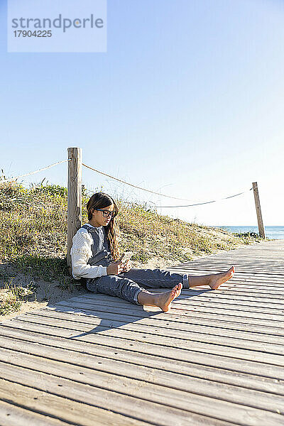 Mädchen sitzt an einem sonnigen Tag mit einem Buch an der Promenade