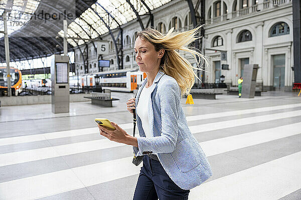 Geschäftsfrau mit Smartphone läuft am Bahnhof