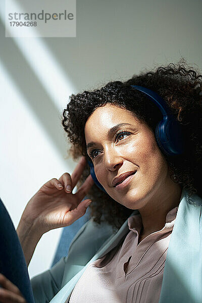 Nachdenkliche Geschäftsfrau hört Musik über kabellose Kopfhörer