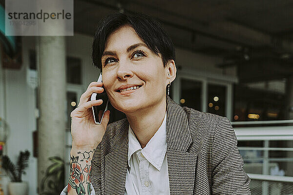 Lächelnde Geschäftsfrau  die im Café mit dem Smartphone spricht