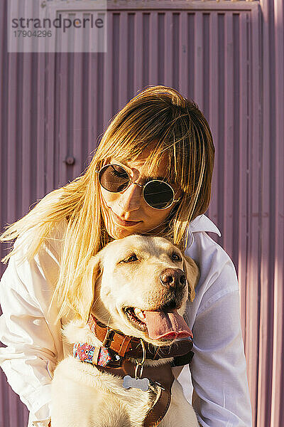Frau mit Sonnenbrille umarmt Hund an sonnigem Tag