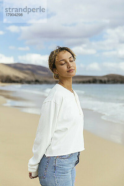 Entspannte Frau mit geschlossenen Augen steht am Strand
