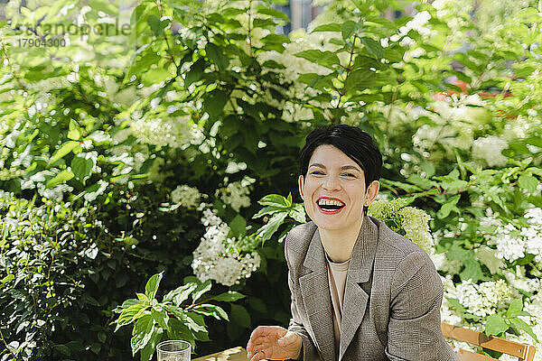 Fröhliche Geschäftsfrau sitzt neben Pflanzen im Café