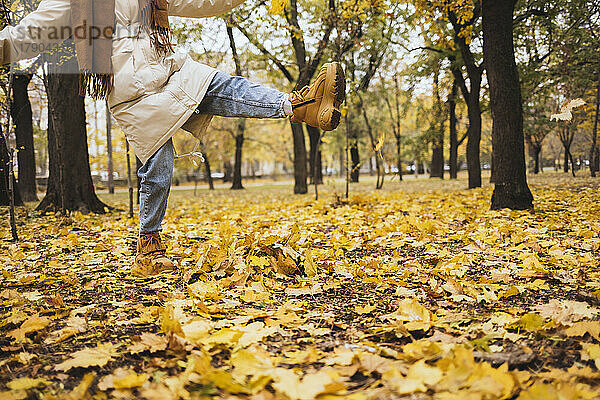 Frau kickt Herbstblätter im Park