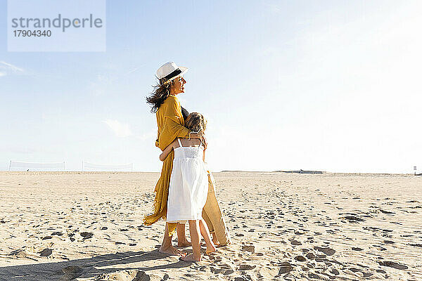 Glückliche Frau umarmt Tochter und Sohn an einem sonnigen Tag am Strand