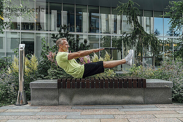 Reifer Mann praktiziert Yoga in Bootsposition auf einer Bank