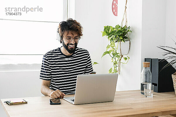 Glücklicher Freiberufler mit Laptop beim Videoanruf im Heimbüro