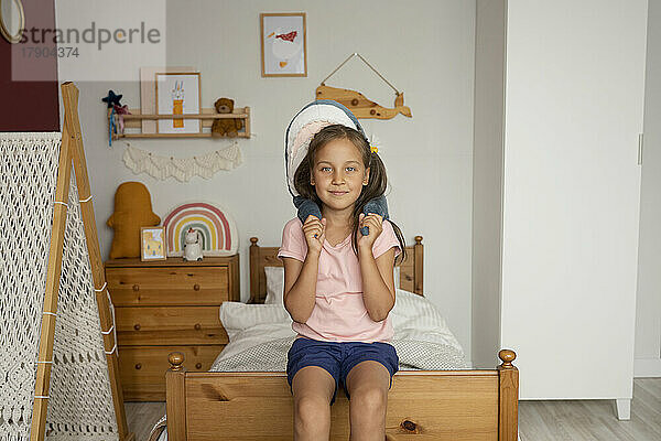 Mädchen mit Spielzeughai sitzt auf dem Bett im Kinderzimmer