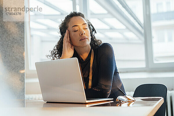 Müder Kundendienstmitarbeiter sitzt mit geschlossenen Augen am Schreibtisch im Büro