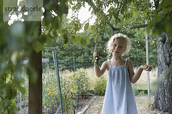 Lächelndes Mädchen hält Pflaumen und Baumstamm im Garten