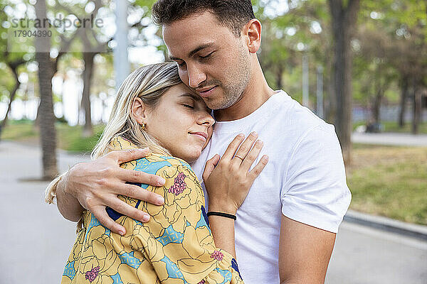 Freund und Freundin umarmen sich mit geschlossenen Augen im Park