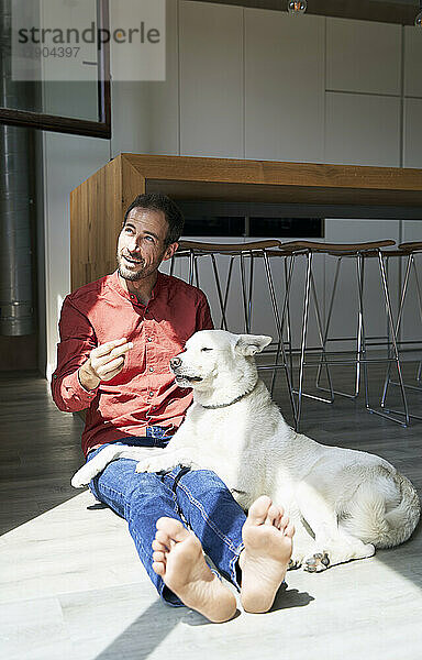Mann gestikuliert  während er an einem sonnigen Tag zu Hause mit Hund sitzt