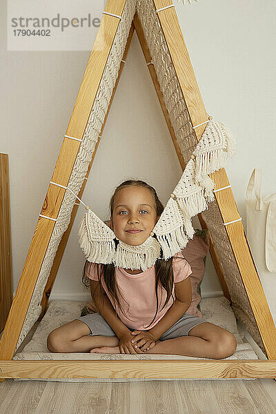 Smiling cute girl sitting in wooden tent at home