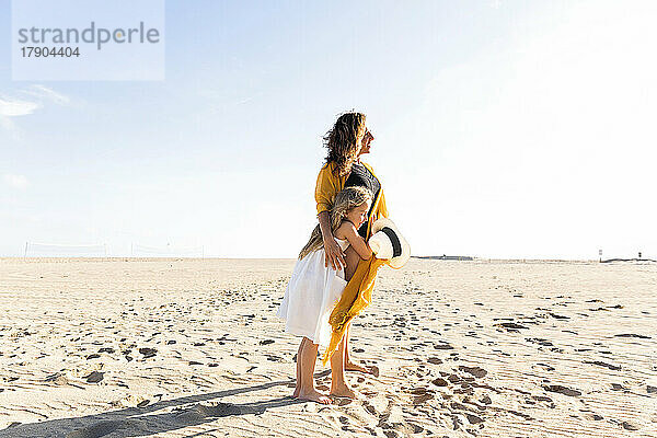 Mädchen umarmt Mutter am Strand an einem sonnigen Tag