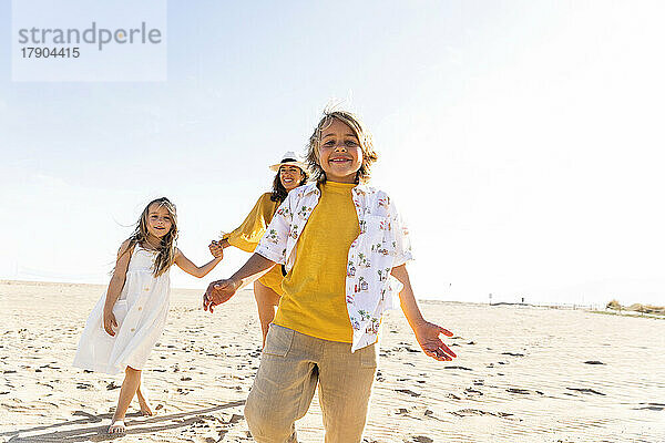 Glücklicher Junge mit Schwester und Mutter  der an einem sonnigen Tag Spaß am Strand hat