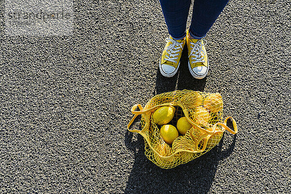 Woman standing by mesh bag with lemons on asphalt