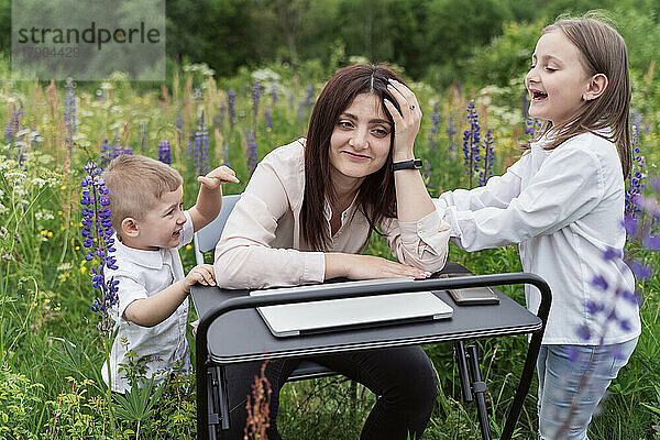 Verspielte Kinder irritieren Mutter  die inmitten von Lupinenblüten sitzt