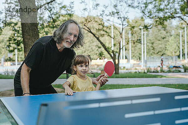 Glücklicher Großvater und Enkelin spielen Tischtennis im Park