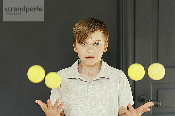 Junge jongliert zu Hause mit Tennisbällen