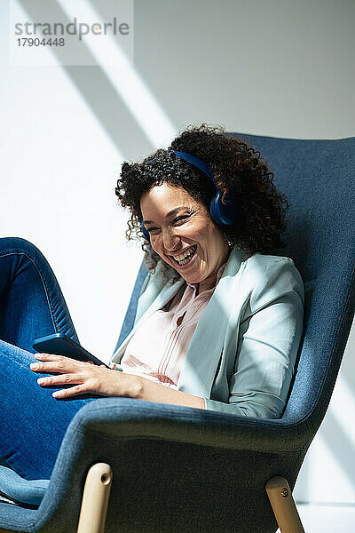 Fröhliche Geschäftsfrau hört im Büro Musik über kabellose Kopfhörer