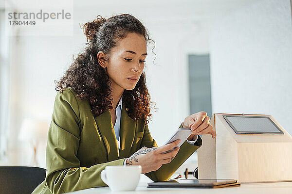 Junge Geschäftsfrau sitzt am Schreibtisch im Büro und nutzt ihr Smartphone