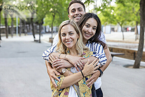 Smiling young man hugging women from behind at park