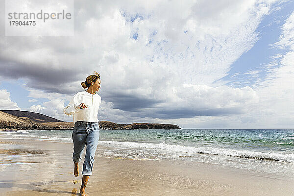 Junge Frau genießt es  an einem sonnigen Tag am Strand zu laufen