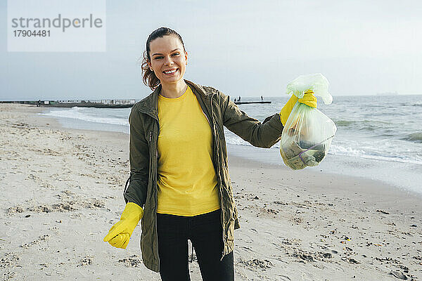 Glücklicher Freiwilliger zeigt Müllsack am Strand