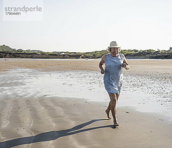 Glückliche ältere Frau  die an einem sonnigen Tag am Strand läuft