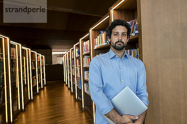 Mann mit Laptop am Bücherregal in der Bibliothek